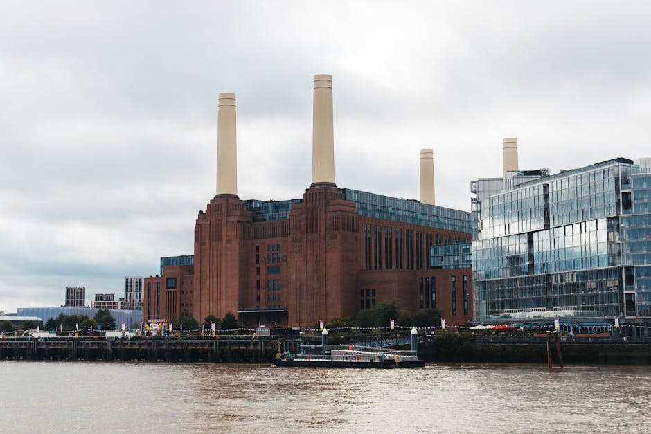 A low-angle view of a modern glass-clad high-rise building with curved, reflective windows on the left, contrasting with the older, large-scale industrial brick building on the right, which features v